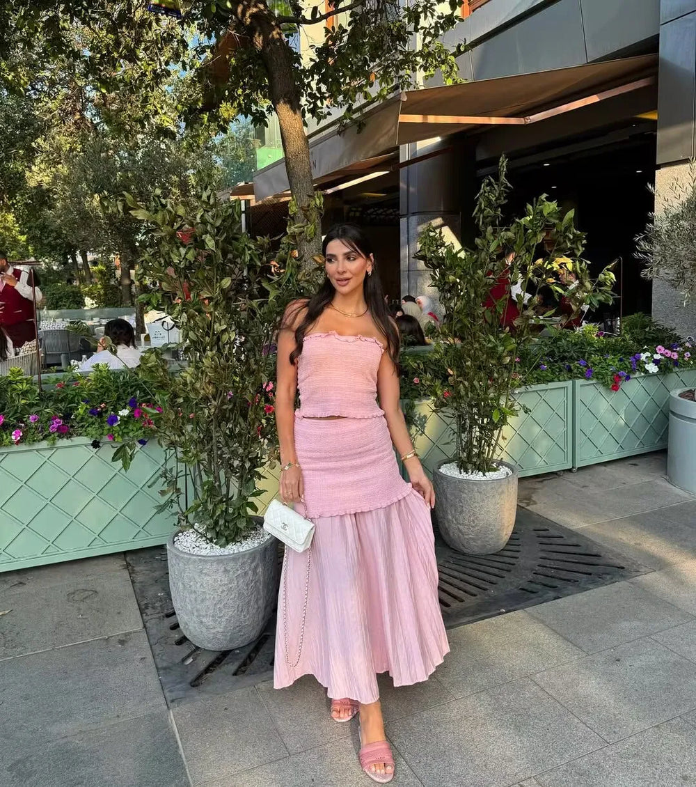 Woman in a pink dress standing outdoors with plants and a building in the background