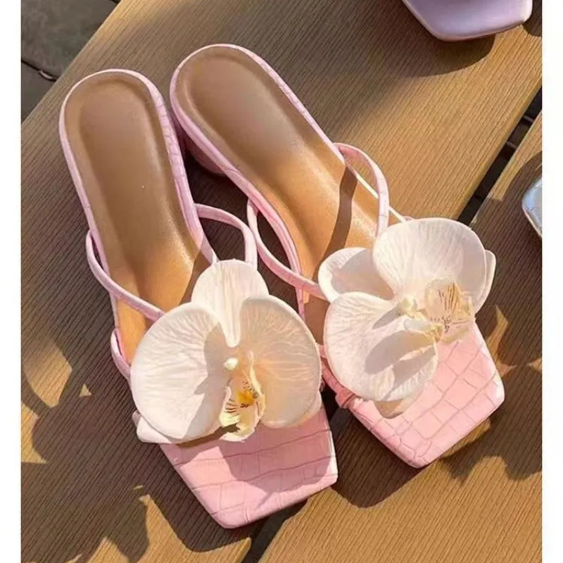 Pink high-heeled shoes with white orchids on a wooden surface