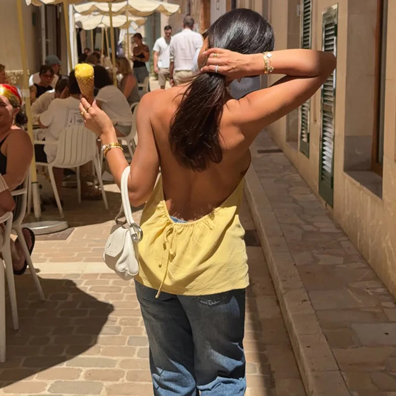 Woman in yellow top and blue jeans standing on a street, holding an ice cream cone.