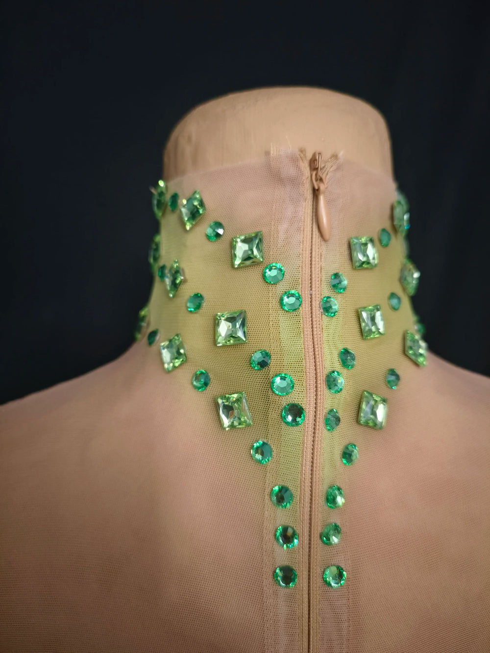 Mannequin wearing a beige garment with green gemstones on a black background