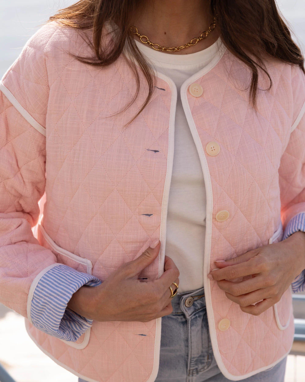 Person wearing a pink quilted jacket with white trim, gold buttons, and a white shirt underneath.
