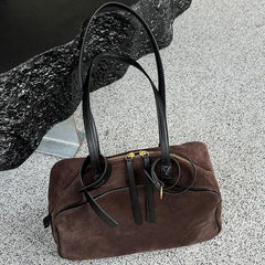 Brown handbag with black straps on a textured surface