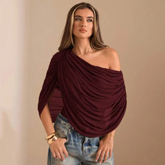 Woman wearing a burgundy off-shoulder top and denim jeans against a beige background