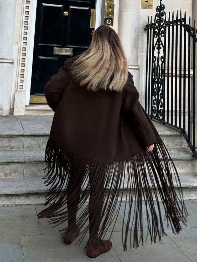 Person wearing a brown fringed coat walking up steps in an urban setting