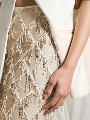 Close-up of a person wearing a beige lace dress with a white jacket.