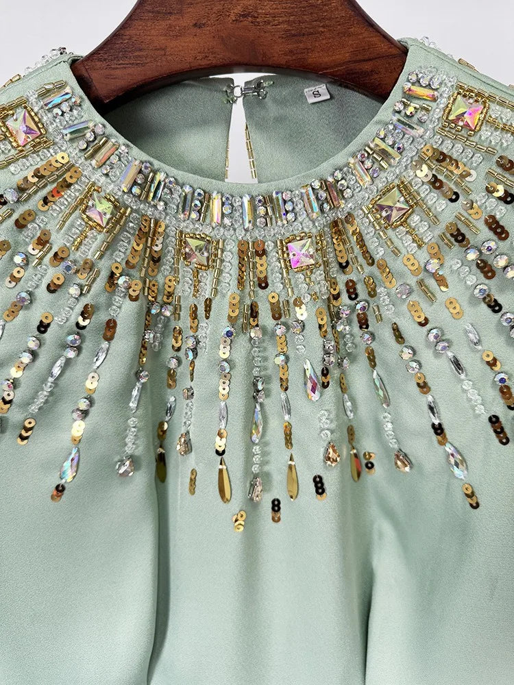Light green blouse with intricate gold and silver beadwork on a wooden hanger.
