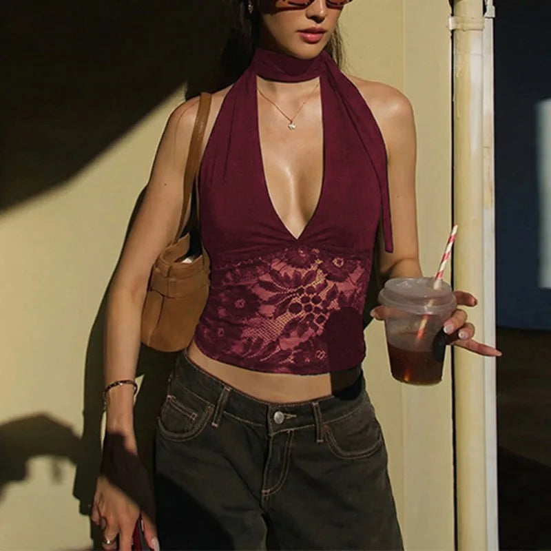 Woman wearing a burgundy lace top and dark jeans, holding a drink.