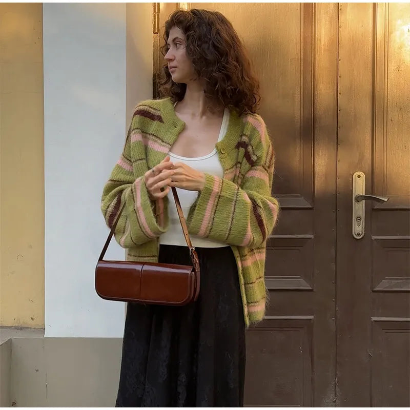 Woman wearing a green and pink striped cardigan holding a brown handbag in front of a door.