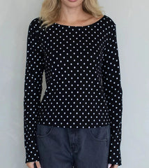 Person wearing a black long-sleeve top with white polka dots against a plain background
