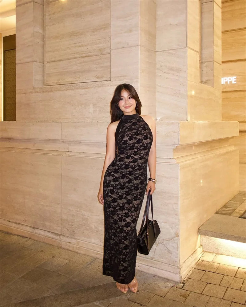 Woman in a black lace dress standing against a stone wall.