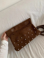 Brown studded clutch held by a hand on a white surface