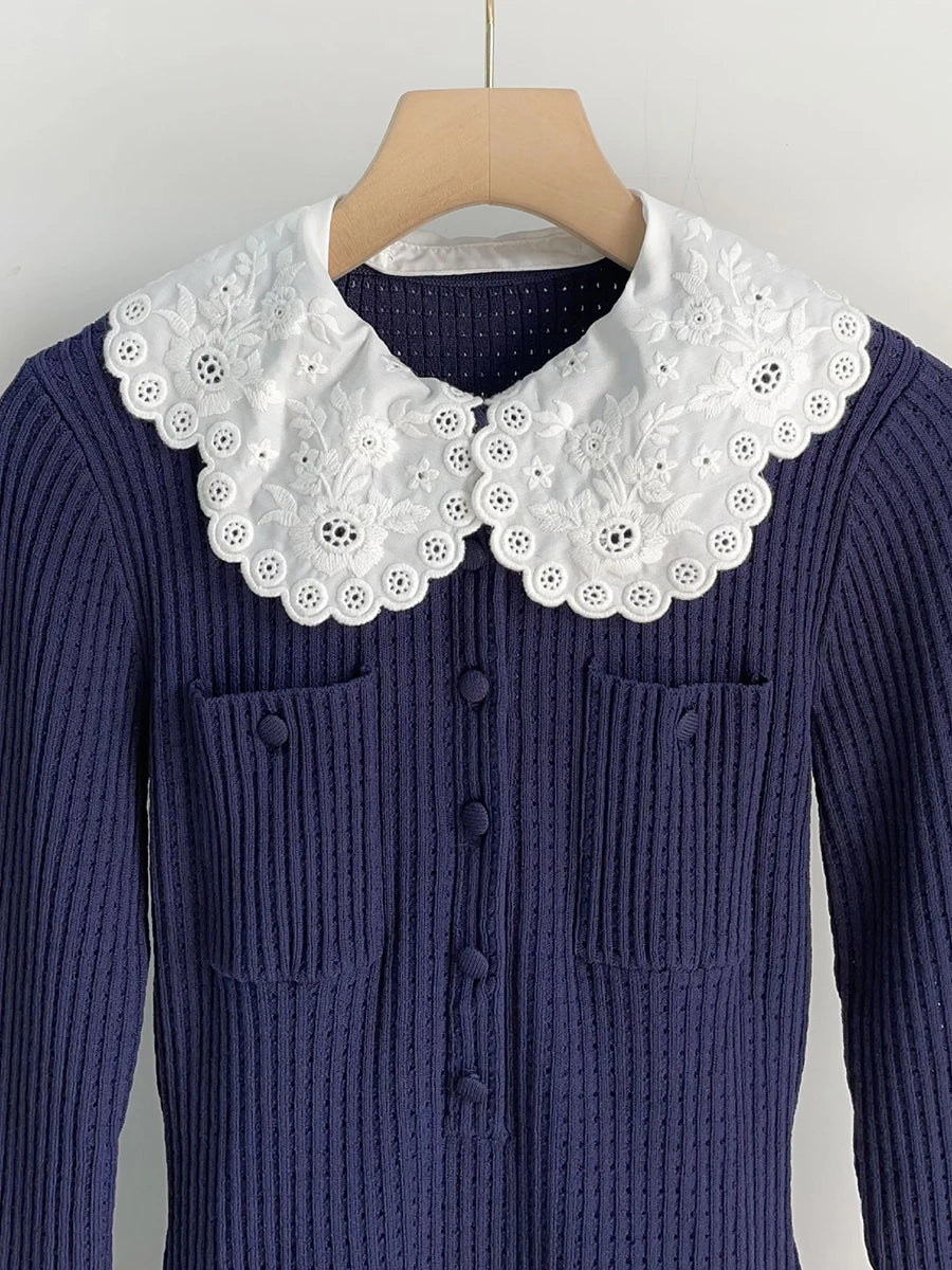 Navy blue ribbed sweater with white lace collar on a hanger against a light gray background