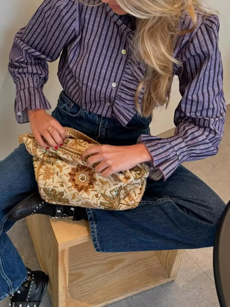 Person sitting on a wooden stool holding a patterned bag.