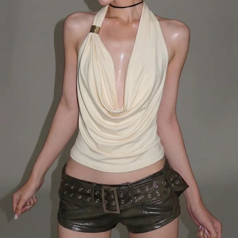 Woman wearing a beige halter top and black leather shorts against a plain background