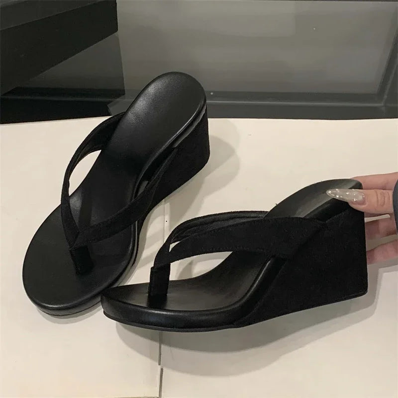 Black wedge sandals on a white surface with a blurred background