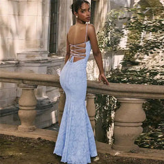 Woman in a light blue lace dress standing by a stone railing with a reflective surface.