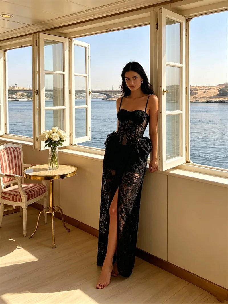 Black lace corset gown with spaghetti straps and a side split, modeled by a woman leaning against a window.