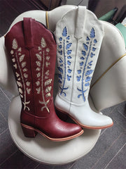 Pair of maroon and white cowboy boots with floral embroidery on a round white surface.