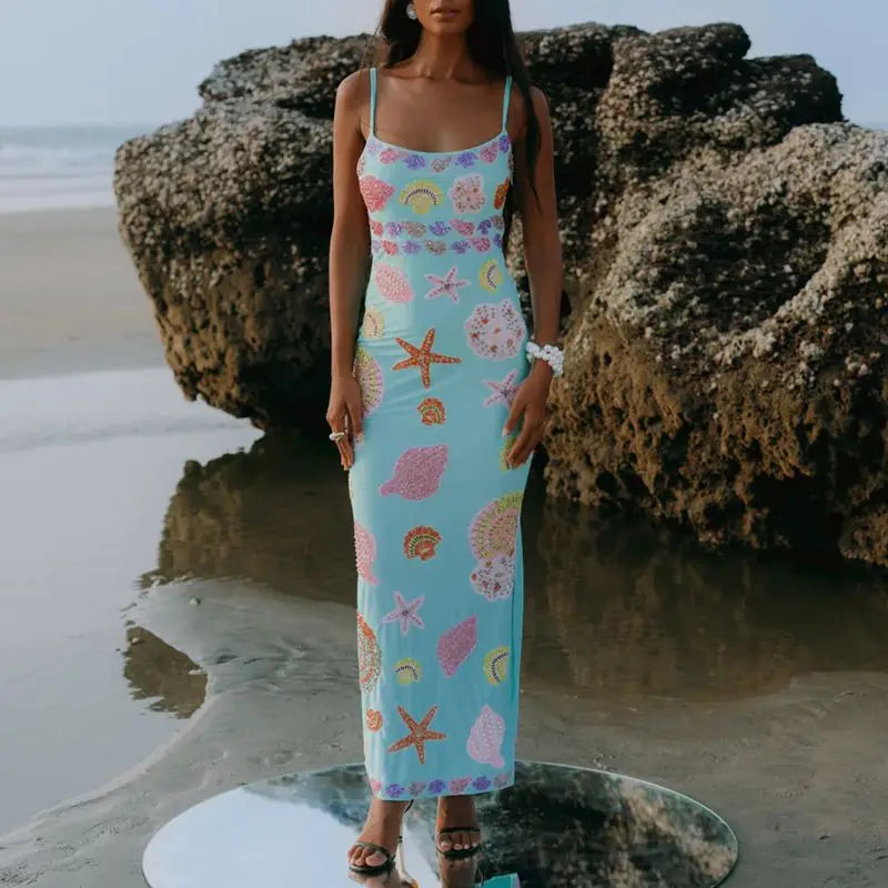 Woman in a floral dress standing on a beach with large rocks.