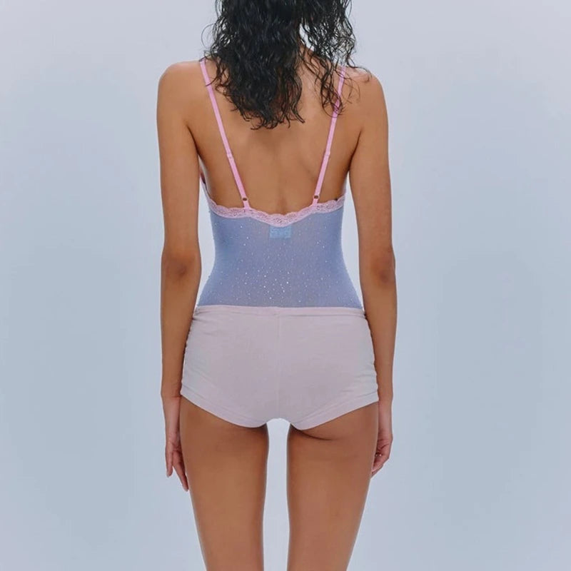 Woman wearing a light blue lace-trimmed bodysuit with pink straps on a plain background
