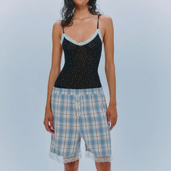 Woman wearing a black polka dot top and plaid shorts on a light blue background