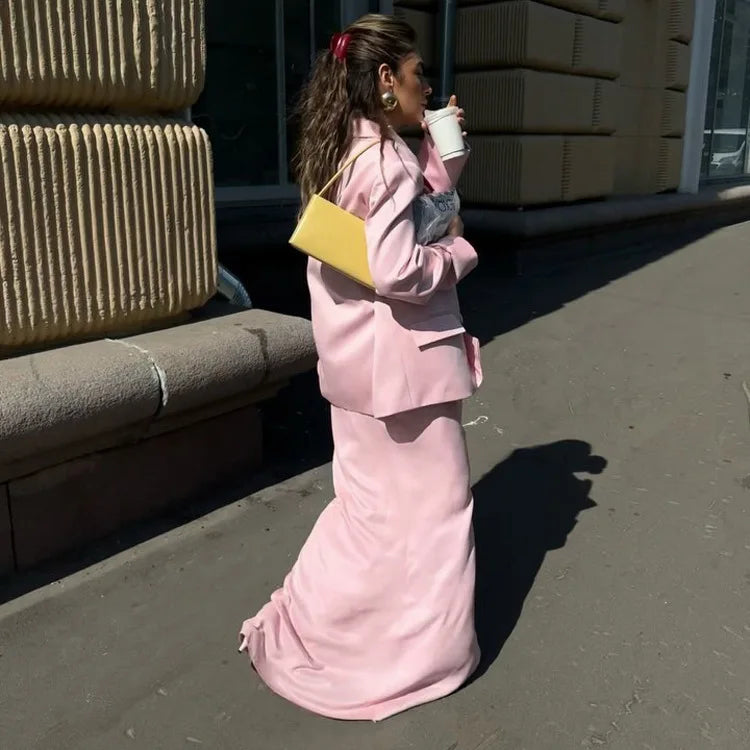 Woman in a pink outfit holding a yellow handbag and a white cup on a sidewalk.