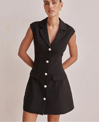Woman wearing a black sleeveless blazer dress with buttons on a plain background