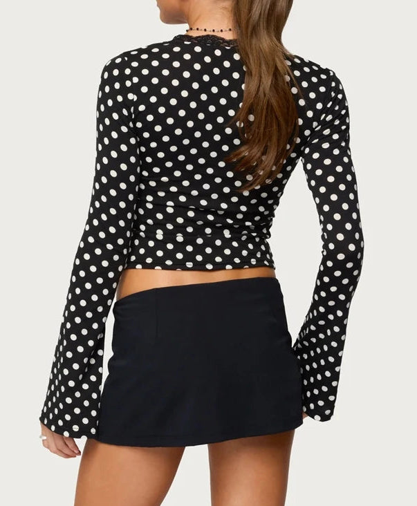 Person wearing a black polka dot long-sleeve top and black skirt on a white background