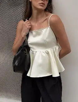 Woman wearing a white satin top and black pants, holding a black handbag against a neutral background.