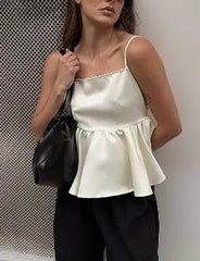 Woman wearing a white satin top and black pants, holding a black handbag against a neutral background.
