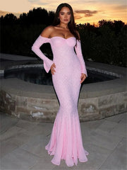 Woman in a pink off-shoulder dress standing by a pool at sunset.