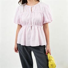 Person styling a pink striped puff sleeve button-front peplum top with grey pants and a yellow bag