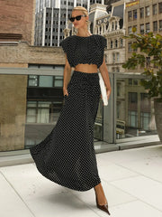 Black polka dot sleeveless crop top and flowing maxi skirt on a woman on a rooftop terrace