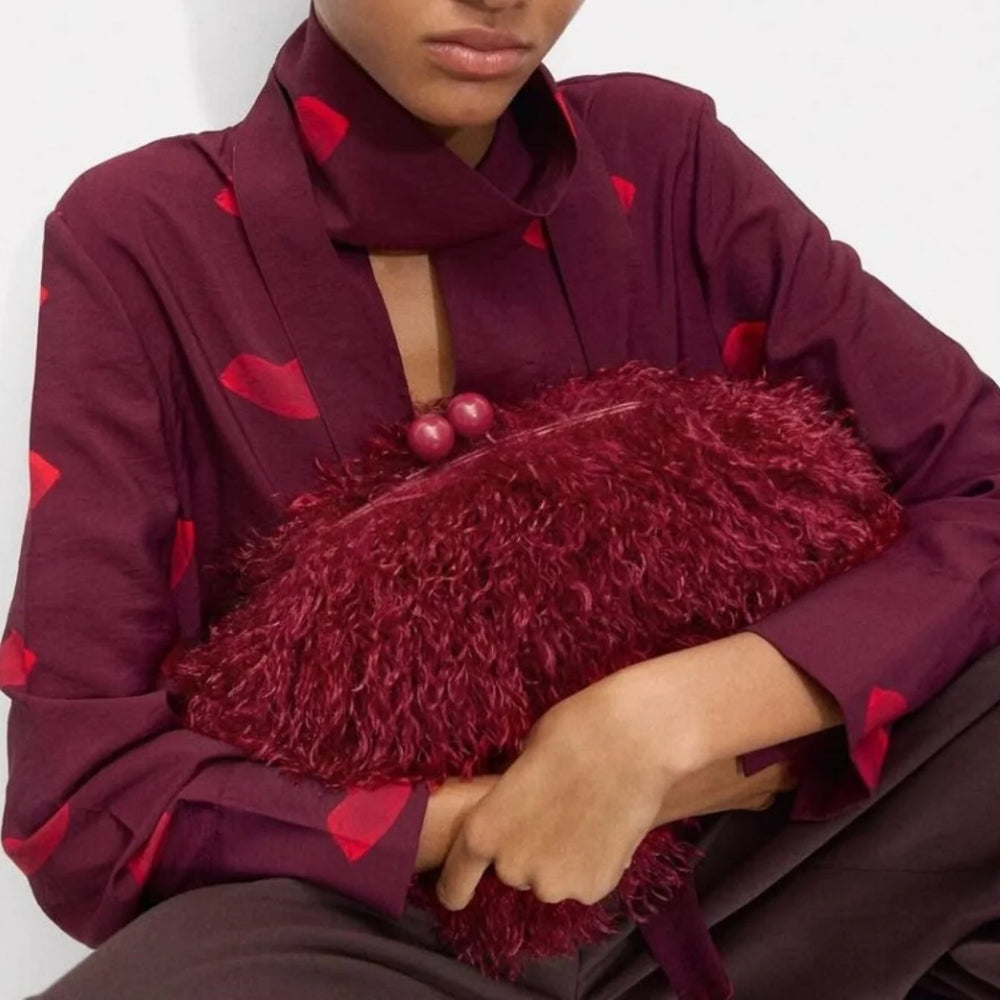 Person wearing a burgundy shirt with red heart patterns holding a textured burgundy clutch.