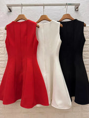 Three dresses in red, white, and black hanging on a rack against a light-colored wall.