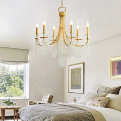 A romantic crystal chandelier with candle-style lights casting a warm glow over a bed room . D