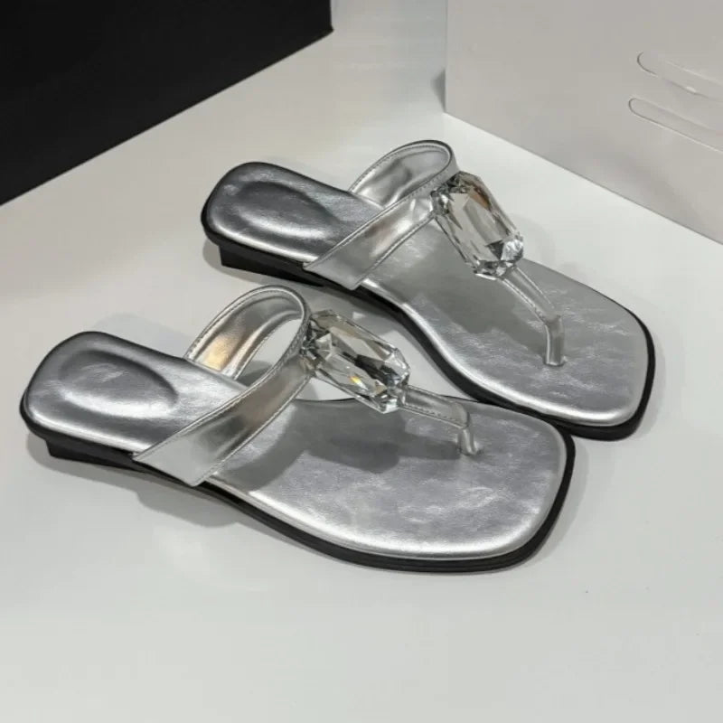 Close-up of silver square toe flat sandals with a crystal accent.