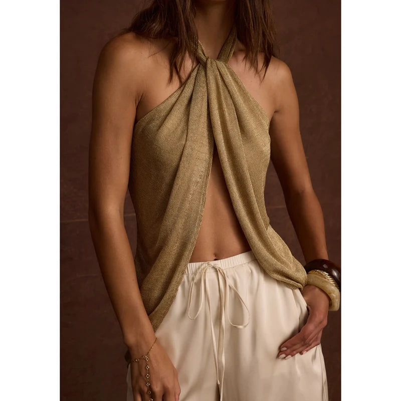Woman wearing a beige halter top with a knot detail and white pants against a brown background