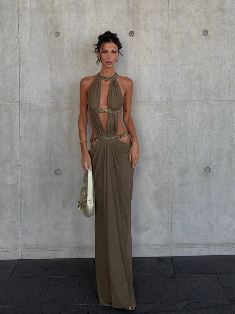 Woman in a long, halter-neck dress standing against a concrete wall.