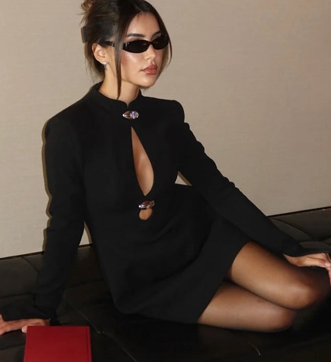 Woman in a black dress sitting on a couch with a red book beside her.