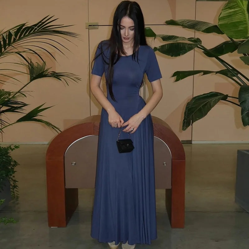 Woman in a blue dress standing in an indoor setting with plants.