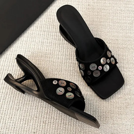 Pair of black square toe wedge heel slide sandals with decorative shell buttons.
