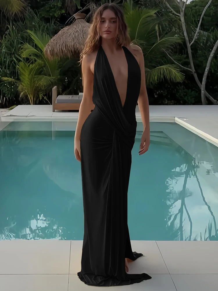 Woman in a black dress standing by a pool with tropical plants in the background