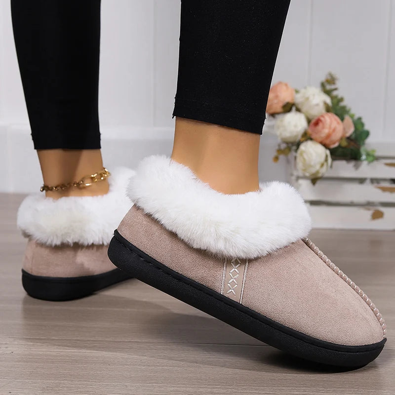 Beige slippers with white fur trim worn indoors on a wooden floor.