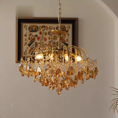 Gold chandelier with crystal accents hanging in a room with a decorative painting on the wall.