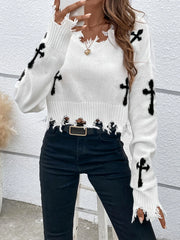 White sweater with black cross patterns worn by a person against a light gray wall.