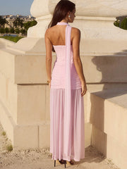 Woman in a pink dress standing against a stone wall with a scenic background