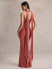Woman wearing a long, elegant rust-colored dress with a draped design on a neutral background