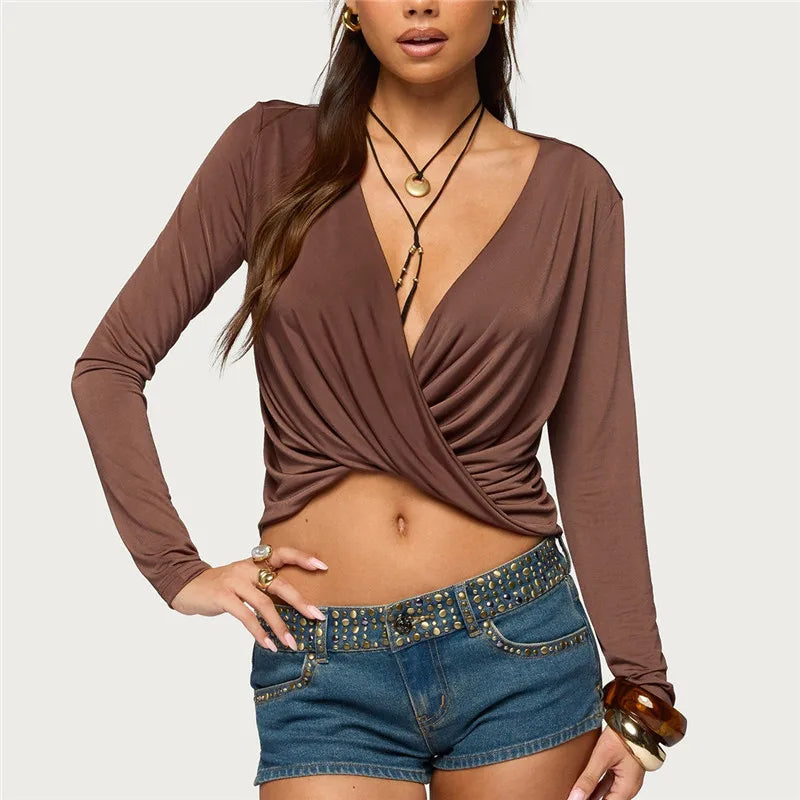 Woman wearing a brown long-sleeve top and denim shorts on a plain background