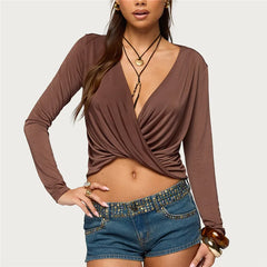 Woman wearing a brown long-sleeve top and denim shorts on a plain background